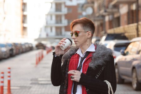 Photo for Outdoors lifestyle fashion portrait of stunning woman. Middle-aged woman drinking coffee and walking on the city street. - Royalty Free Image