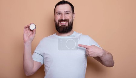 Handsome bearded man presenting beard balm on beige background