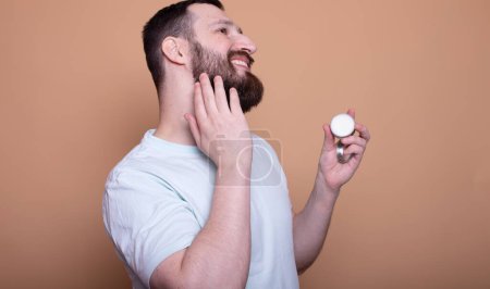 Téléchargez les photos : Beau barbu homme présentant baume de barbe sur fond beige - en image libre de droit