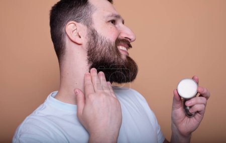 Handsome bearded man presenting beard balm on beige background