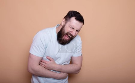 Photo for Young bearded man suffering from stomach pain isolated on beige background - Royalty Free Image