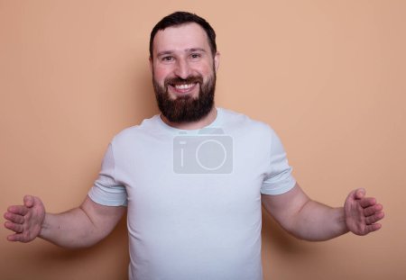 Foto de Guapo barbudo con estilo confiado hombre mostrando espacio de copia en blanco sobre fondo beige - Imagen libre de derechos