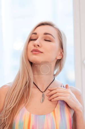 Photo for Portrait of blonde woman in colorful rainbow hippie top and boho necklace accessories near window - Royalty Free Image