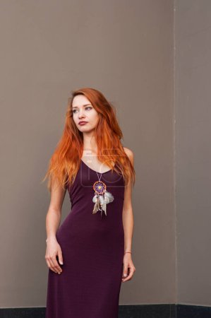Photo for Portrait of beautiful slim redhead girl in wine boho chic dress and handmade white dreamcatcher feather talisman pendant - Royalty Free Image