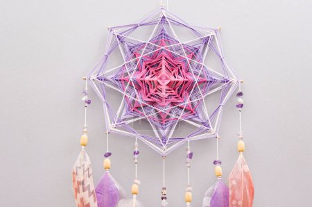 Photo for Handmade esoteric woven mandala magical dreamcatcher with feathers and amethyst gemstone on grey background, meditation tool for yoga room interior - Royalty Free Image