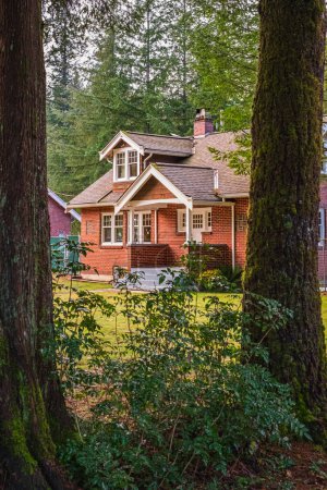 Téléchargez les photos : Belle maison unifamiliale en brique rouge avec herbe verte et grands arbres. Grande maison avec véranda entourée par une belle nature. Personne. mise au point sélective, photo de rue - en image libre de droit