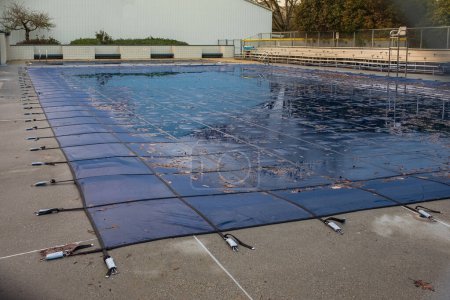 Photo for Swimming pool with cover from dirt. Public swimming pool with pool slide tarped up and closed down for winter. Pool with winter cover for autumn. Nobody, street photo - Royalty Free Image