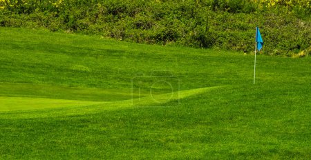 Foto de Poner verde con una bandera en un campo de golf en un día de verano. Campo de golf en el campo. enfoque selectivo, nadie, espacio de copia. Campo de golf con un rico césped verde hermoso paisaje - Imagen libre de derechos