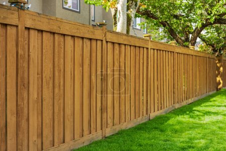 Téléchargez les photos : Belle nouvelle clôture en bois autour de la maison. Clôture brune en bois avec pelouse verte. Photo de rue, personne, mise au point sélective - en image libre de droit