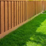 Nice new wooden fence around house. Wooden brown fence with green grass lawn. Street photo, nobody, selective focus