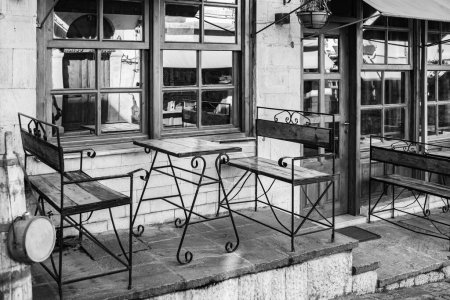 Téléchargez les photos : Terrasse de café à l'ancienne en noir et blanc. Vieille rue confortable à Gjirokaster Albanie. Café extérieur avec tables et chaises en bois. Personne, photo de rue, mise au point sélective - en image libre de droit
