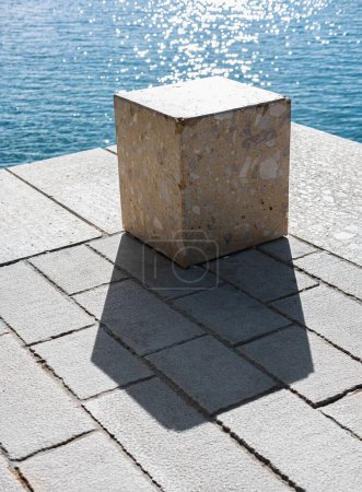 Foto de Cubo de hormigón o ladrillo de cemento con sombra. Foto abstracta. Cubo de piedra primer plano con el mar azul en el fondo. Masivo cubo de tierra. Nadie, foto de la calle - Imagen libre de derechos