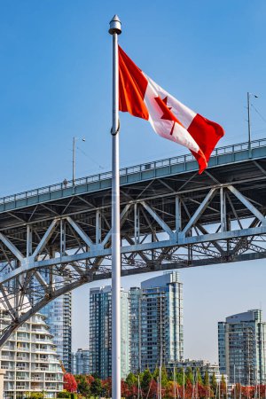 Foto de Bandera canadiense con el centro de Vancouver en segundo plano. La ubicación es Granville Island. Bandera de Canadá frente a False Creek y el puente de la calle Burrard en Vancouver, Canadá - Imagen libre de derechos