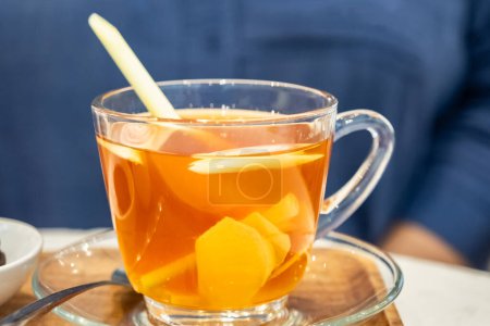 Téléchargez les photos : Tasse de thé au gingembre avec citronnelle et miel. Coupe en verre de thé au gingembre chaud avec racine de rhizome de gingembre tranchée. Herbes et épices. Thé au gingembre sain - en image libre de droit