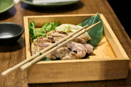 Chicken yakitori served in a wooden box and on top of it your Japanese chopsticks (hashi)