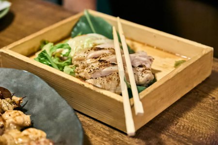 Chicken yakitori served in a wooden box and on top of it your Japanese chopsticks (hashi)