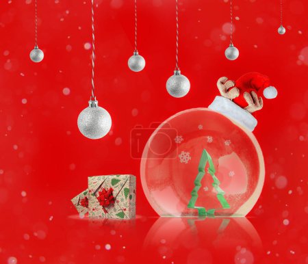 Foto de Bola transparente con árbol verde y sombrero de Santa Claus, cajas de regalo sobre fondo rojo abstracto. Fondo de Año Nuevo festivo para carteles y tarjetas. - Imagen libre de derechos