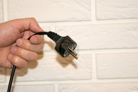 Photo for View of a hand holding a black 220v plug against a white brick wall - Royalty Free Image