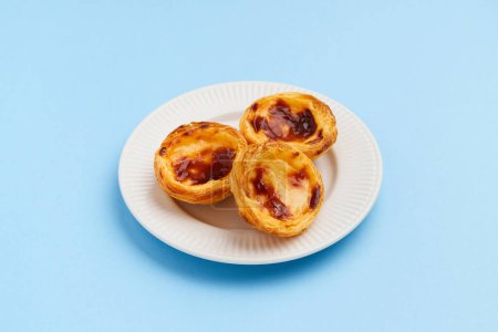 Photo for Traditional Portuguese egg tart dessert Pasteis Pastel de nata or Pastels de Belem on the plate over blue background. Local pastry cafeteria concept - Royalty Free Image