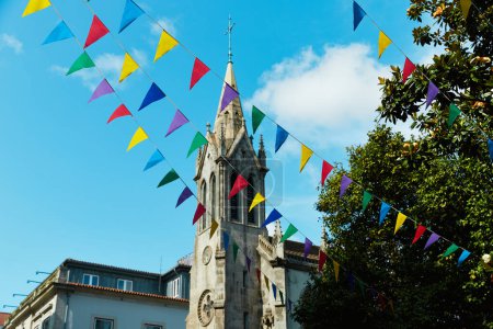 Colorful flags before an old church tower against a blue sky for summer festival in June San Juan, Portugal