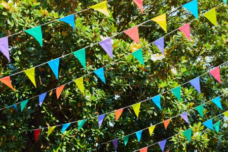 Bunte Fahnen hängen vor sattgrünem Laub für das Sommerfest im Juni in San Juan, Portugal