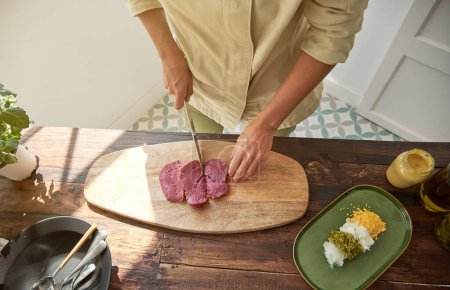 Photo for Top view of professional female chef cutting beef with knife in process of cooking steak tartare in kitchen at home - Royalty Free Image