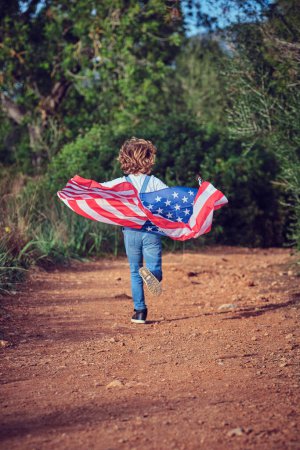 Photo for Full body back view of anonymous active boy running with colorful USA flag on rural path in countryside with green trees - Royalty Free Image