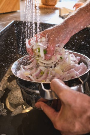 Photo for Hands of crop anonymous person rinsing fresh chopped onion in colander in sink under water while cooking in light kitchen - Royalty Free Image