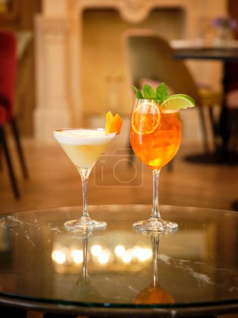 Foto de Vaso de Aperol Spritz y Whiskey Sour cócteles sobre mesa de mármol en bar moderno - Imagen libre de derechos