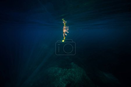 Téléchargez les photos : Plongeur mâle lointain méconnaissable dans des nageoires jaunes nageant sous l'eau bleu foncé d'eau profonde pendant les vacances - en image libre de droit
