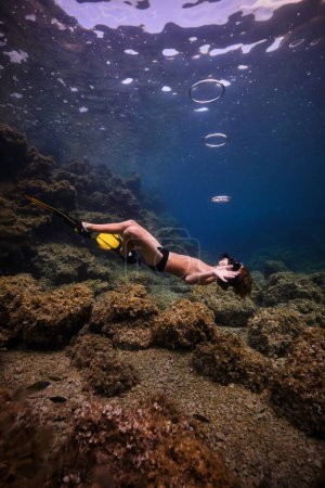 Foto de Vista lateral cuerpo completo de hombre sin camisa joven anónimo en máscara de snorkel y aletas nadando bajo el agua clara del océano cerca de los arrecifes de coral a la luz del día - Imagen libre de derechos