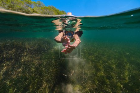 Foto de Vista submarina de niño irreconocible en máscara de snorkel nadando en el mar profundo durante las vacaciones de verano - Imagen libre de derechos