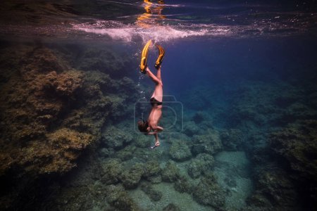 Téléchargez les photos : Vue latérale du plongeur mâle méconnaissable dans les nageoires et masque nageant sous l'eau de la mer près des récifs coralliens - en image libre de droit
