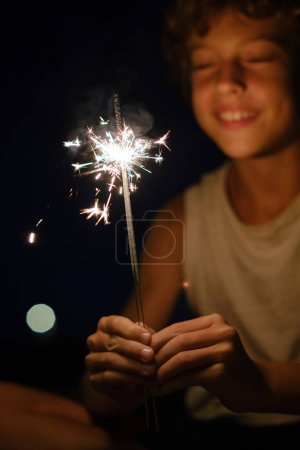 Foto de Alegre niño preadolescente borroso con luces de Bengala brillantes que celebran el evento festivo por la noche - Imagen libre de derechos