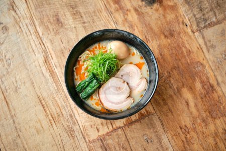 Photo for Top view of appetizing fresh cooked ramen with pork and creamy broth served in black bowl on wooden table in restaurant - Royalty Free Image