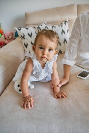 Téléchargez les photos : D'en haut de adorable petite fille en vêtements décontractés assis sur le canapé et regardant la caméra - en image libre de droit
