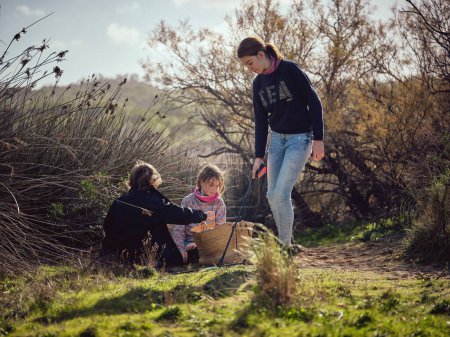 Téléchargez les photos : Vue latérale de l'adolescente à la recherche d'ordures et de déchets plastiques avec accaparement des ordures dans un pré herbeux tout en participant à un mouvement écologique avec des amis - en image libre de droit