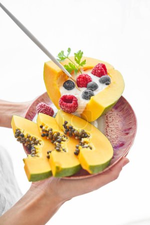 Photo for Unrecognizable person demonstrating portion of sweet dessert made of papaya raspberries blueberries and yogurt and served on pink ceramic plate with spoon - Royalty Free Image