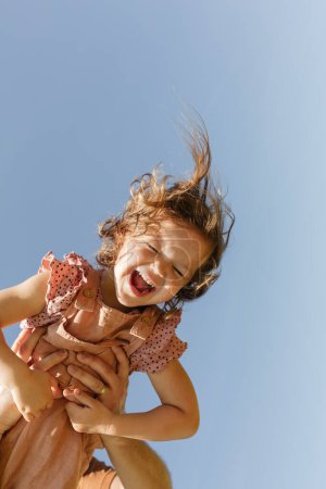 Foto de Bajo ángulo de anónimo sosteniendo feliz niño feliz poco divertirse juntos en el día soleado contra el cielo azul sin nubes - Imagen libre de derechos