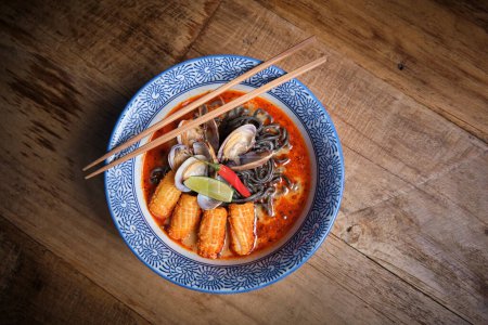 Photo for Typical hot ramen dish with fish broth in a bowl with black noodles, squid, chilli, clams. - Royalty Free Image