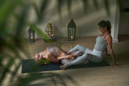 Téléchargez les photos : Vue latérale des athlètes féminines en vêtements de sport assis sur le tapis et faisant des exercices d'étirement ensemble pendant l'entraînement de yoga dans le studio moderne - en image libre de droit