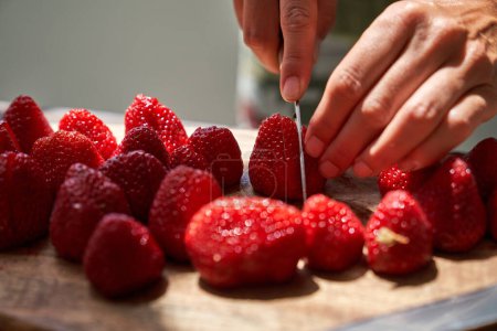Foto de Persona irreconocible cortando frutas frescas de fresa orgánica dulce madura en la tabla de cortar con cuchillo - Imagen libre de derechos