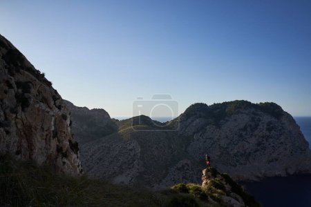 Téléchargez les photos : Randonneur masculin avec sac à dos debout au sommet de la colline et observer des paysages pittoresques spectaculaires avec des montagnes et la mer - en image libre de droit