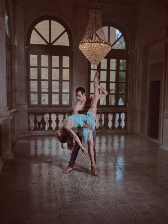 Téléchargez les photos : Femme en pointe flexion dans le stand divisé avec support de danseuse dans la salle de bal intérieur sous lustre - en image libre de droit
