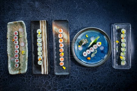 Foto de Vista superior de varios rollos maki servidos en varias placas de mármol en la mesa de mármol azul - Imagen libre de derechos