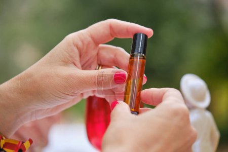 Téléchargez les photos : Mains féminines montrant une petite bouteille d'huile de beauté sur fond flou à l'extérieur - en image libre de droit