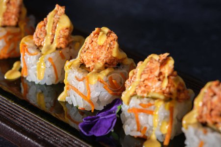 Téléchargez les photos : Du dessus de sushis appétissants garnis de saumon et de sauce fraîche servis sur une assiette en bois au restaurant sur fond noir - en image libre de droit