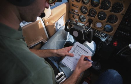 Photo for High angle crop attentive male aviator sitting in helicopter first officers seat and ticking in pilots checklist - Royalty Free Image