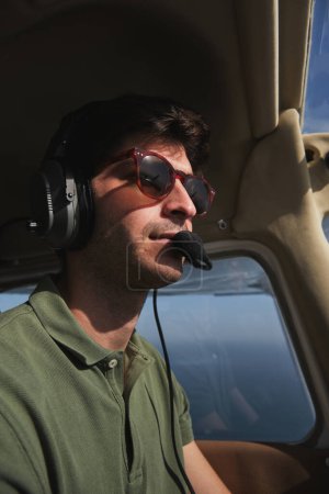 Foto de Foto en stock del hombre concentrado con auriculares de aviación que pilota aviones ligeros. - Imagen libre de derechos