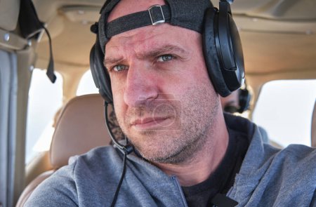 Photo for Crop thoughtful adult male captain in headphones and casual wear riding modern airplane on sunny day - Royalty Free Image